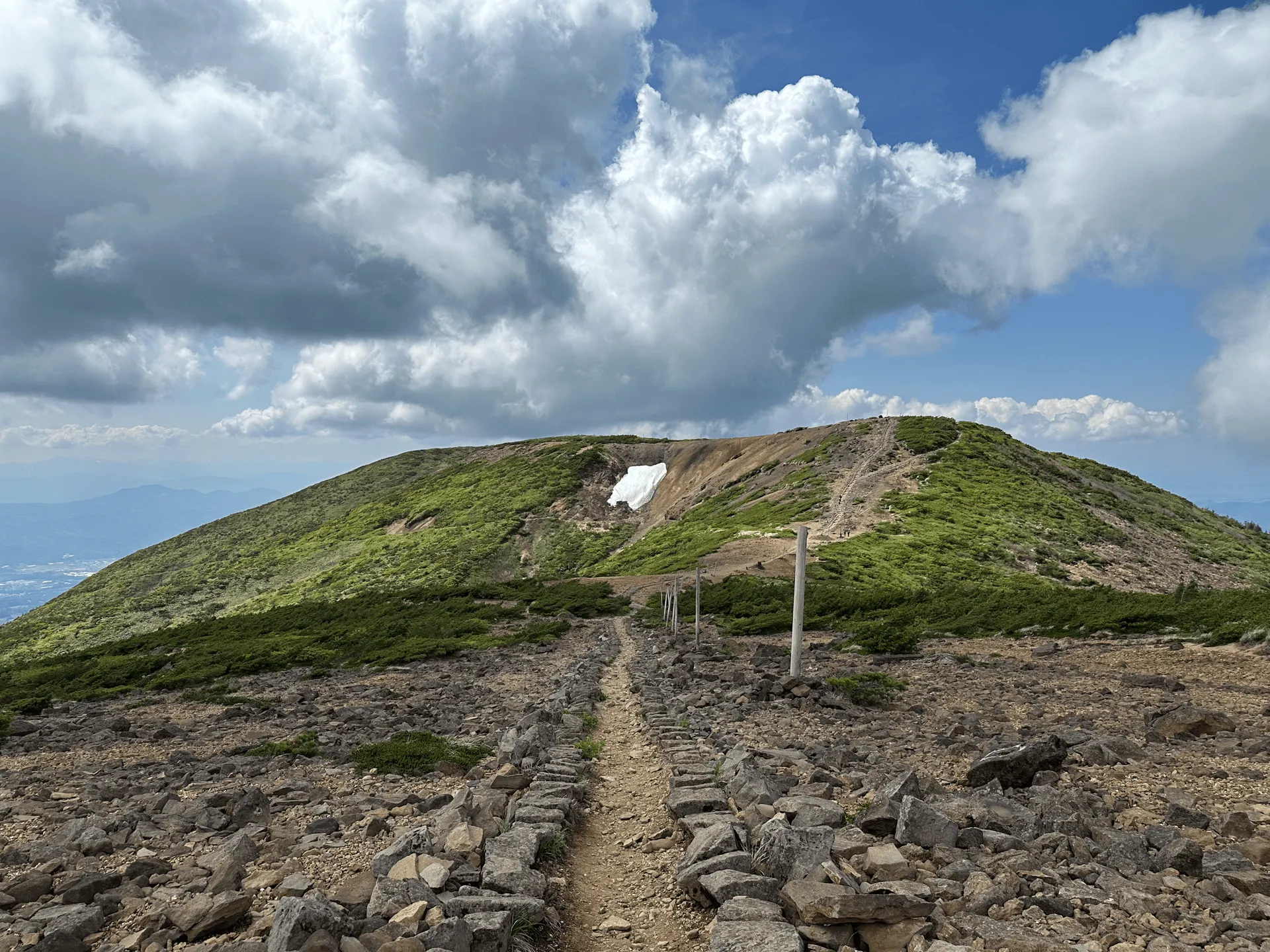 A dirt trail, fenced by rocks on either side, leading up to a green hill.